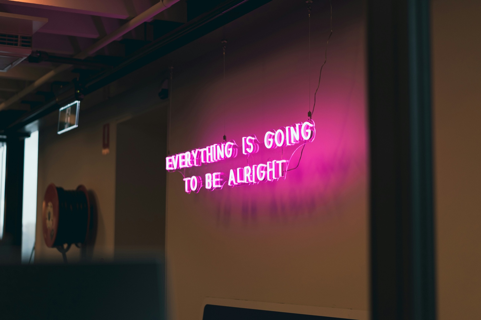 Neon sign reading 'Everything is going to be alright' in a modern workspace